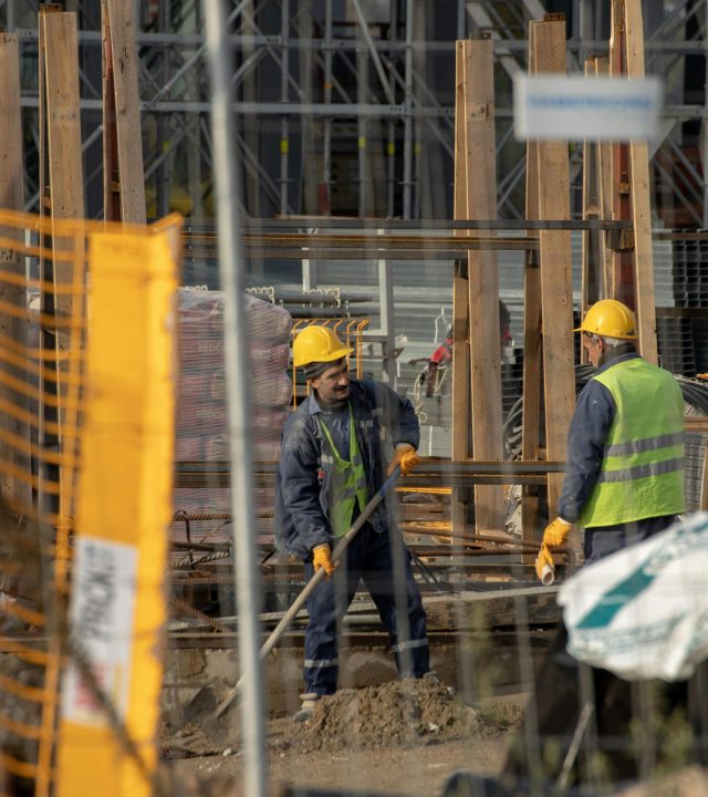 Construction workers in hard hats at an active building site with safety barriers.